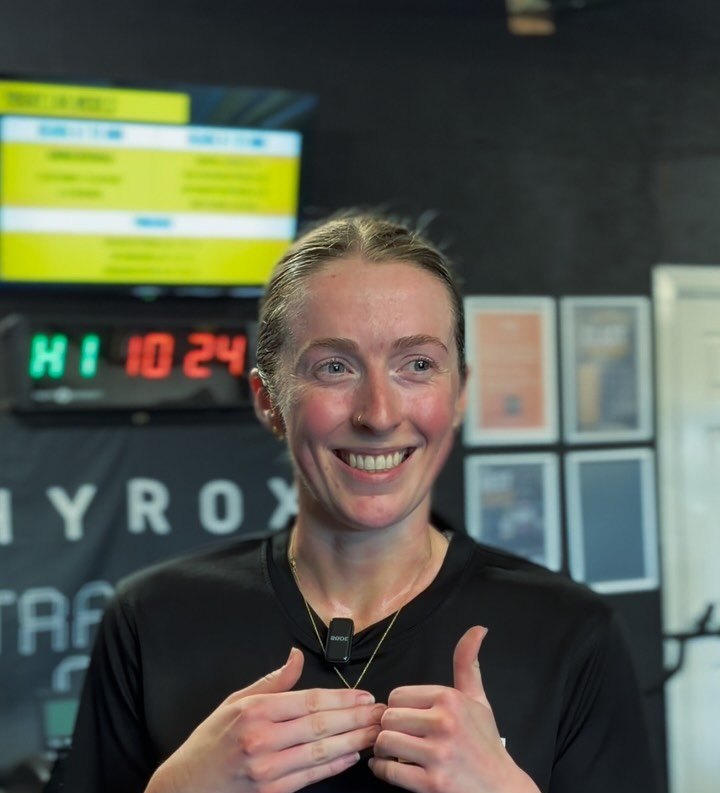 A LIFT coach in a LIFT tee in the studio, workout screens behind